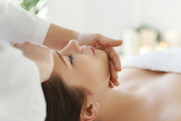 Beautician doing face massage of young beautiful relaxed woman in spa salon