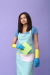 Portrait of a middle age woman in blue gloves  holding in her hands cleaning  cloth while standing on a purple background.