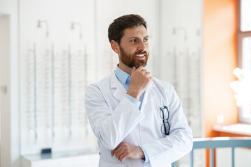 Portrait of smiling ophthalmologist in front of showcase in optics store looks away