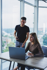 Two colleagues are discussing work on a laptop. Friendly relations in the office between colleagues. Workflow in the office