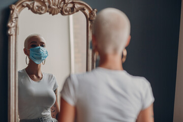 Wall Mural - Millenial young woman in medical protective face mask with short blonde hair portrait standing at mirror indoor