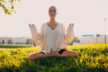 Wall Mural - Portrait of young millenial european short haired woman doing yoga lotus asana on green grass meadow summer park sunset. Beautiful happy blonde girl outdoor.