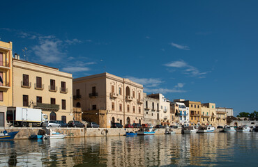 The banks of the Mazaro River in Mazara del Vallo, Italy. The houses are reflected in the water. In the background the blue sky with small white clouds.