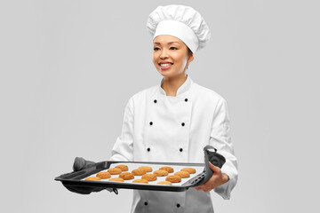 Sticker - cooking, culinary and bakery concept - happy smiling female chef or baker in toque holding baking tray with oatmeal cookies over grey background