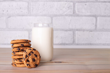 Composition of freshly baked homemade biscuits with chocolate chips. Healthy breakfast concept with glass of milk and cooked cookies on wooden table for overlay on product presentation.