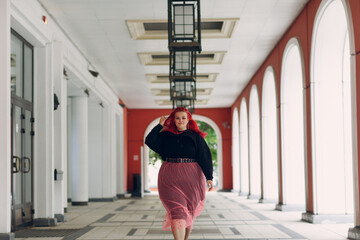 Wall Mural - European plus size woman walking outdoor street city. Young red pink haired body positive girl.