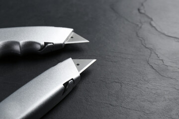 Canvas Print - Two utility knives on black table. Space for text