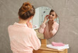 © New Africa - Beautiful woman wearing pink bathrobe in front of mirror at home