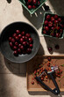 © The Picture Pantry - Pints of fresh red cherries being pitted into a dark bowl on a tile surface in hard light.