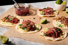 Five Pork Tacos With Pickled Red Onions Laid Out On Parchment Paper.