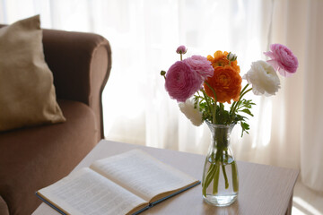 Bouquet of beautiful ranunculus flowers in vase and open book on wooden table indoors. Space for text