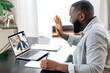 Online video meeting. African American young successful man talking on video conference with his colleague, friend or mentor while sitting at the desk in the office, talking about strategy,takes notes