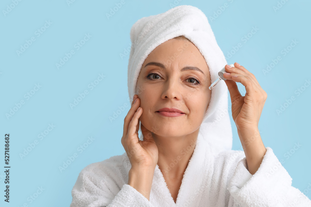 Mature woman with cosmetic serum on blue background
