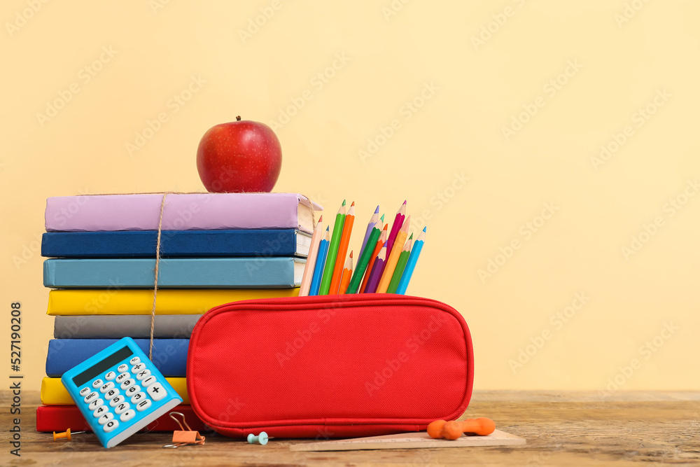 Red pencil case with school stationery and apple on table against beige background