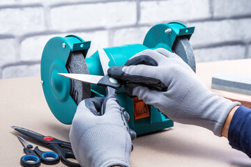 Male hands in gloves sharpening a scissors.