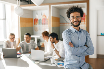 Portrait of smiling businessman standing in modern office on colleagues background