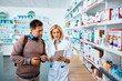 © Drazen - Female pharmacist using touchpad while assisting male customer in pharmacy.