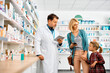 © Drazen - Mature pharmacist talks to mother and daughter in pharmacy.