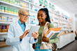 © Drazen - Senior pharmacist and young black woman using touchpad in pharmacy.