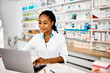 © Drazen - Young black pharmacist using laptop while working in pharmacy.