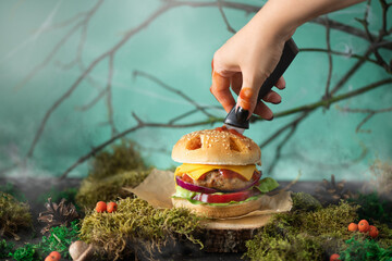 Halloween burger in a shape of pumpkin head jack lantern in a mystery forest. Scary cheeseburger on halloween party.