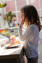 Girl Wearing White Sweater Licking Her Finger With Peanut Butter Jar And Bread On A Plate