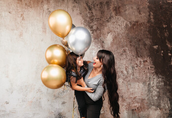 Charming mom and little daughter in the same outfit pose together after a birthday party. Portrait of a charming girl hugging her daughter. balloons