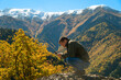 © yaroslav1986 - Young male tourist blogger is sitting on a slope with a mobile phone in his hands against the background of mountains on an autumn sunny day