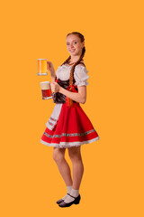 sexy oktoberfest waitress dressed in traditional dirndl (dirndl) dress serving big mug of beer on yellow background

