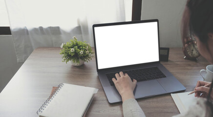 Wall Mural - Mockup image of a woman using and typing on laptop with blank white desktop screen on wooden table