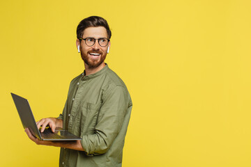 Remote job concept. Happy man with laptop in hands looking aside at copy space, standing on yellow background