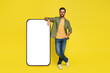 Full body length of man leaning on big smartphone with empty white screen, standing on yellow studio background, mockup