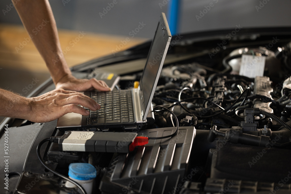 Auto mechanic uses laptop while conducting diagnostics test. Modern car ...
