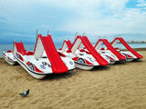 Fototapeta Sypialnia - Group of plastic pleasure catamarans with slides of red and white color stand on an empty sandy beach in a seaside resort on evening.