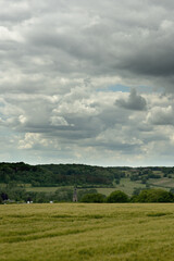 Wall Mural - Rolling countryside with a church and some houses under a cloudy sky.