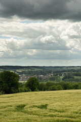 Wall Mural - Rolling countryside with a village and church under a cloudy sky.