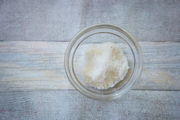 Bowl of salt on gray wooden background, top view