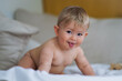 © shellygraphy - super sweet naked almost one year old happy blond baby boy lying at home on a cozy bed after bathing in prone position and smiling or flirting with the Camera like a innocent rascal