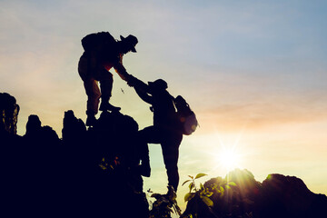 Silhouette climbing buddies help each other climb up the mountain at sunrise as the right lifestyle idea