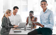 © Jesse B/peopleimages.com - Portrait of a happy businessman smile with a tablet in a team planning meeting at work. An employee in an office with his team as they discuss strategy or plans, and strategies in a corporate office