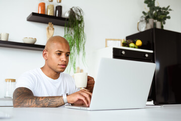 African american entrepreneur holding cup and using laptop in kitchen 