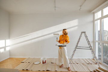 Wall Mural - Portrait of a young woman making repairing in apartment, standing with paint roller near ladder in bright room of her new home