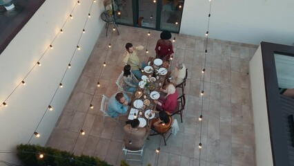 Wall Mural - Family and friends celebrating at dinner on a rooftop terrace. Multiethnic group of people dining on the balcony on a special evening to celebrate friendship and family love and relationships