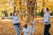 Portrait Of A Family With Children Tossing Autumn Leaves In Park In Autumn. Family Portrait Of Four Members, Father, Mother And Children. Family Concept.