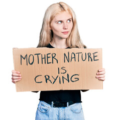 Poster - Young caucasian woman holding mother nature is crying protest cardboard banner smiling looking to the side and staring away thinking.