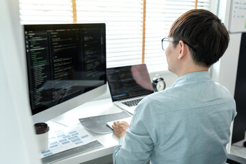 Male programmer is programming to develop program app and website of corporate while working to checking program code and debugging on multiple screen at modern software office