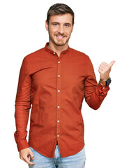 Handsome caucasian man wearing casual clothes smiling with happy face looking and pointing to the side with thumb up.