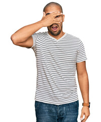 Canvas Print - Hispanic adult man wearing casual clothes peeking in shock covering face and eyes with hand, looking through fingers with embarrassed expression.