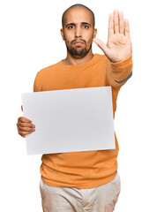 Canvas Print - Hispanic adult man holding blank empty banner with open hand doing stop sign with serious and confident expression, defense gesture