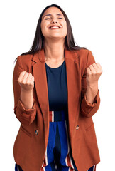 Canvas Print - Young beautiful brunette woman wearing elegant clothes very happy and excited doing winner gesture with arms raised, smiling and screaming for success. celebration concept.